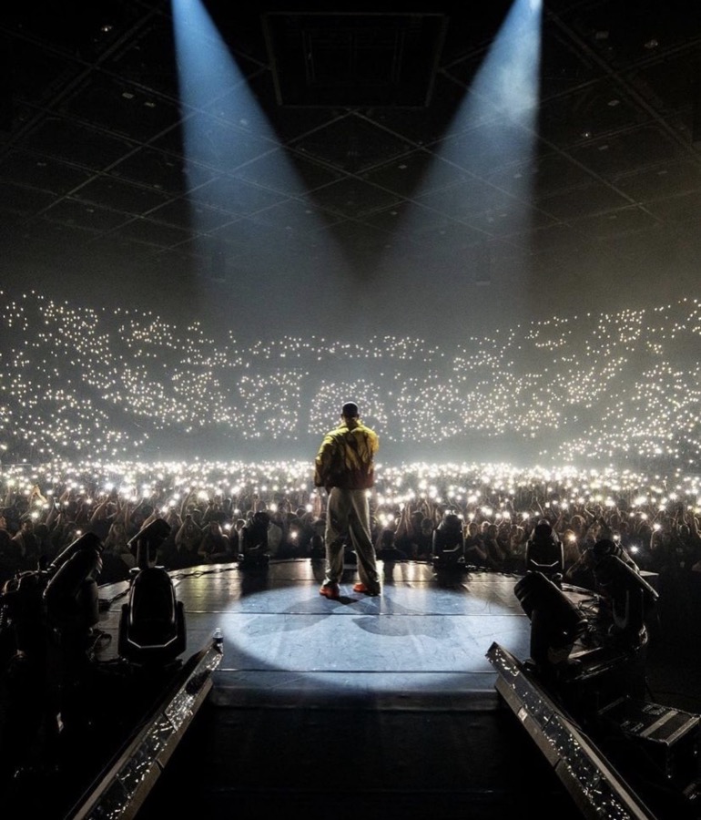 A performer lit on a circular stage in front of a packed arena